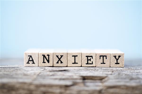 The word "Anxiety" spelled out in Scrabble tiles on a wood table with a blue background