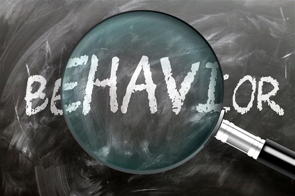  Behavior written in white on a chalk board, magnifying glass enlarging the center of the text